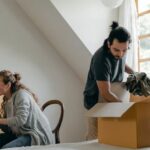 Attic Home - Ethnic boyfriend unpacking box while woman using laptop at home