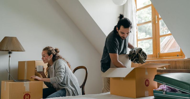 Attic Home - Ethnic boyfriend unpacking box while woman using laptop at home