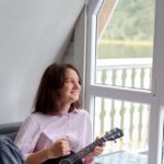 Attic Home - Smiling woman playing ukulele on couch in countryside house