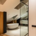 Attic Bathroom - Interior of modern bathroom with wooden elements near entrance and bright illumination over bathtub